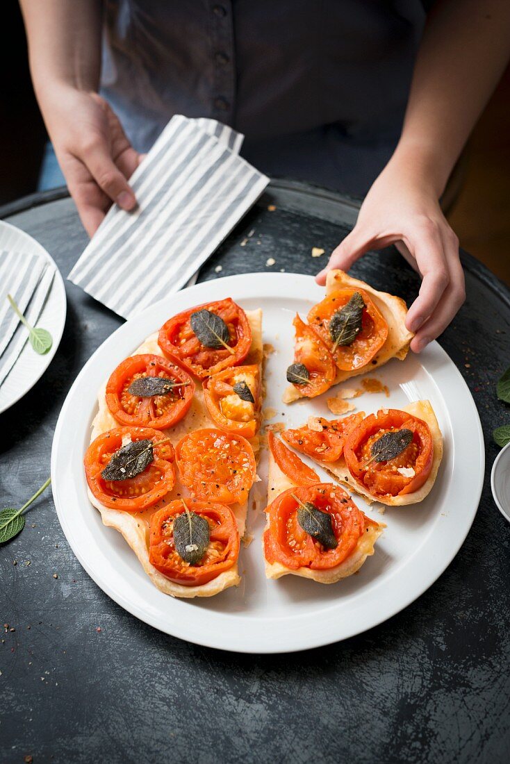 A hand reaching for a piece of tomato tart with sage on a plate