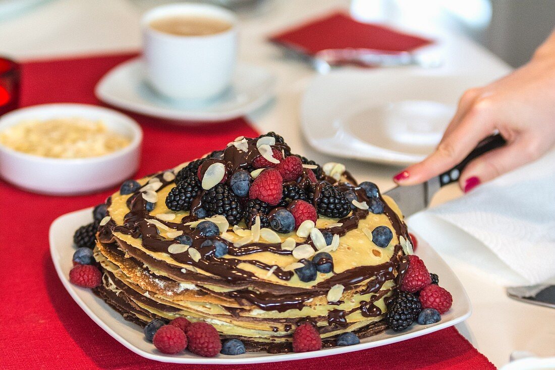 A pancake cake with berries and chocolate sauce being sliced