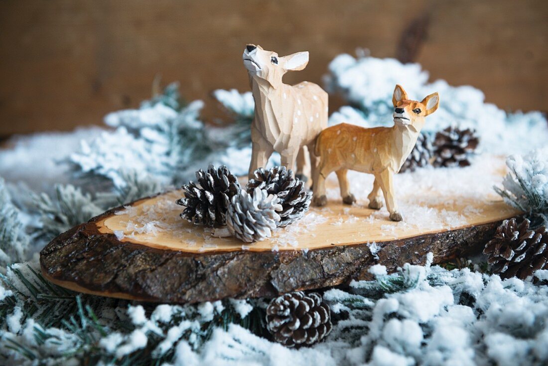 Weihnachtsdeko mit geschnitzten Rehfiguren auf Holzscheiben und verschneiten Zweigen