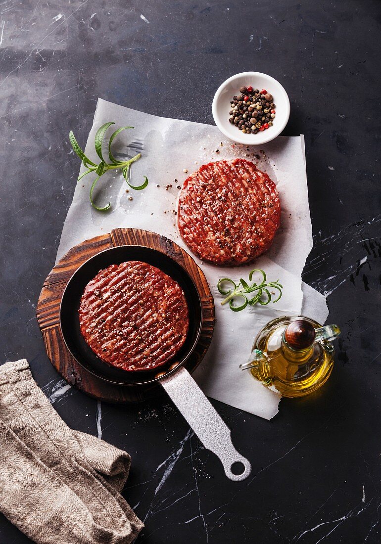 Raw Ground beef meat Burger steak cutlets and seasonings on dark marble background