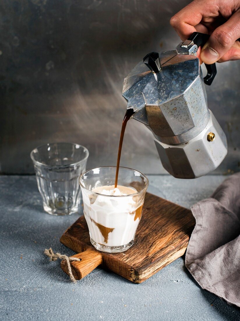Eiskaffee zubereiten: Espresso wird aus Espressokanne in Glas mit Milch und Eis gegossen