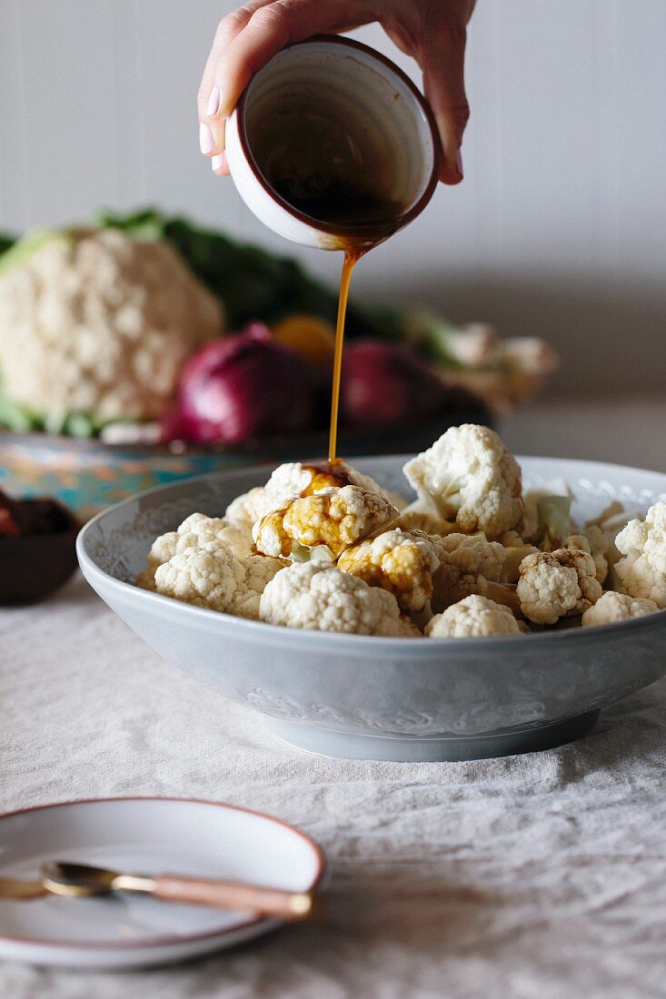 Raw cauliflower florets are being drizzled with a spicy dressing by a person