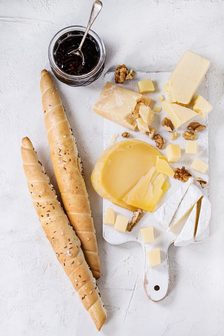 Cheese plate, assortment of cheese with walnuts, jam and bread on white wood serving board