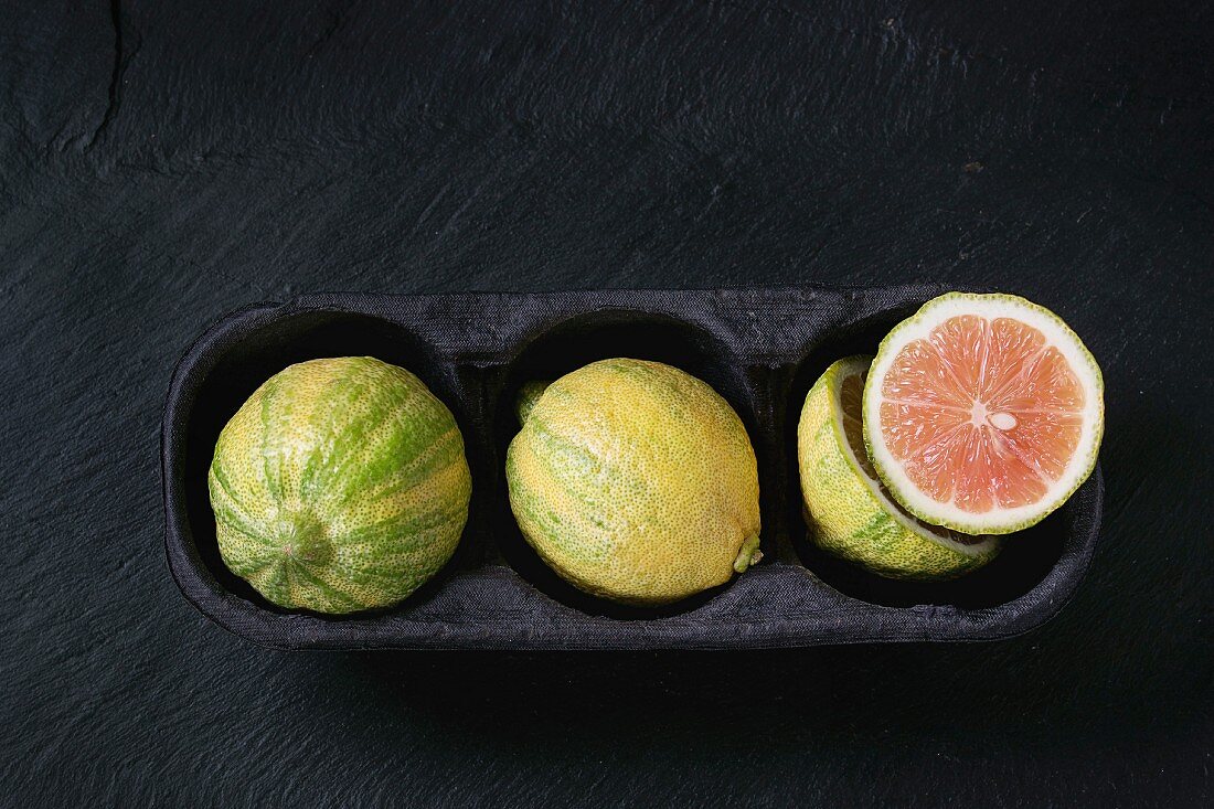 whole and sliced citrus fruit pink tiger lemon in paper market box over black stone slate textured background