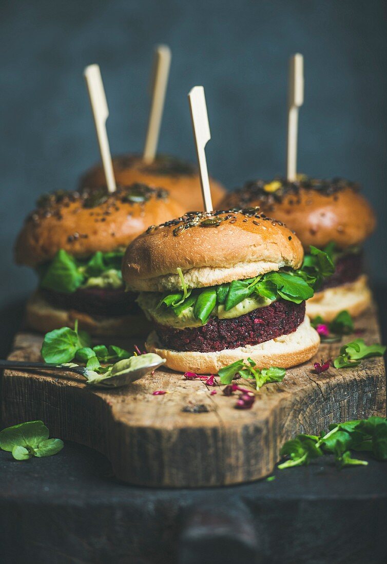 Healthy vegan burger with beetroot and quinoa patty, arugula, avocado sauce and wholegrain buns on rustic wooden board