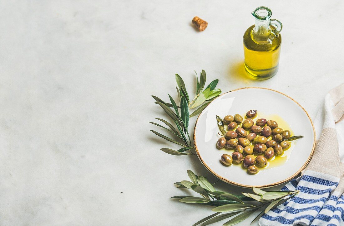 Eingelegte grüne Oliven auf Teller, daneben Olivenölflasche und Olivenzweige