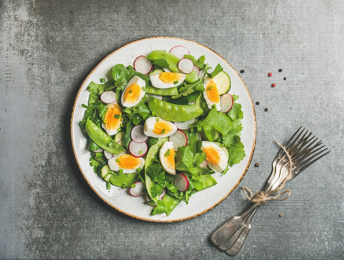 Healthy spring green salad with radish, boiled egg, arugula, green pea and mint in white plate