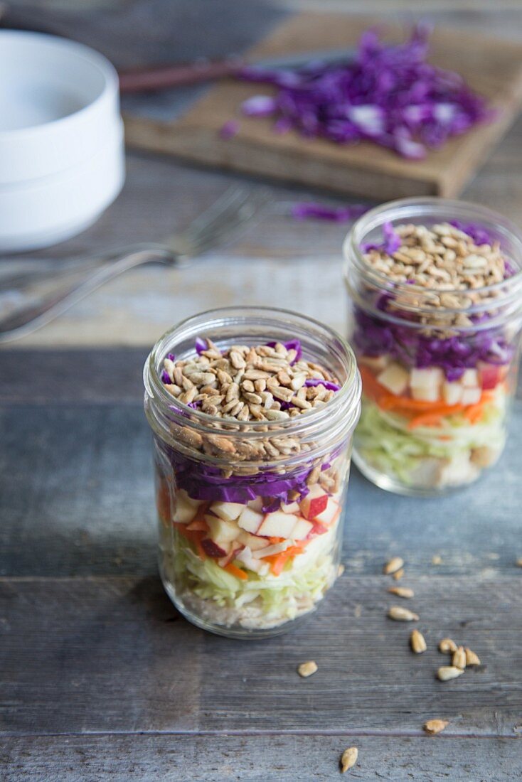 Layered salad with chicken, carrots, apple, red cabbage, white cabbage and sunflower seeds in a jars