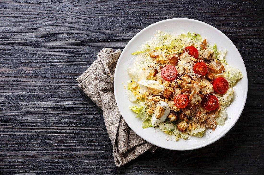 Caesar salad with chicken breast on dark wooden background copy space