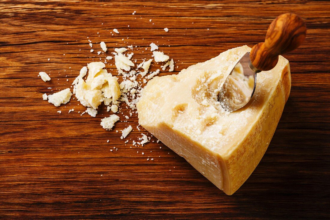 Ein Sttück Parmesankäse mit Käsemesser auf Holzuntergrund