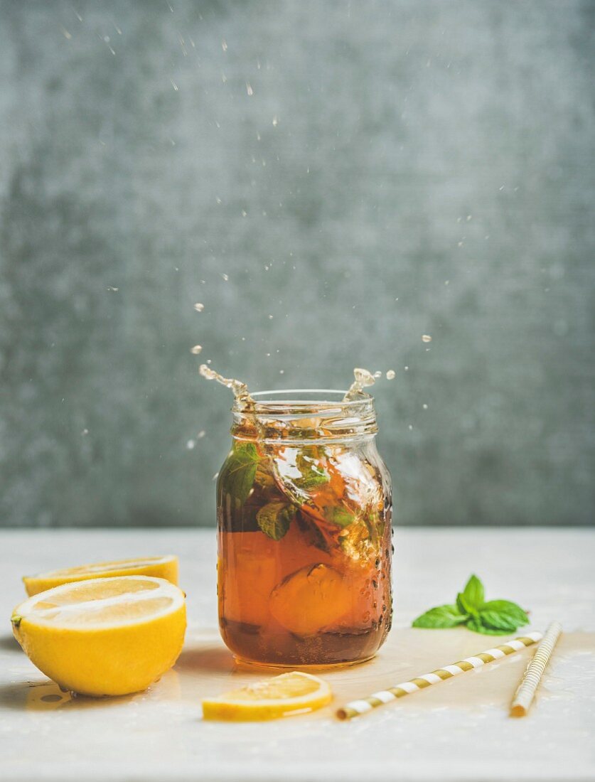 Summer cold Iced tea with fresh bergamot, mint and lemon in glass jar with splashes on light table