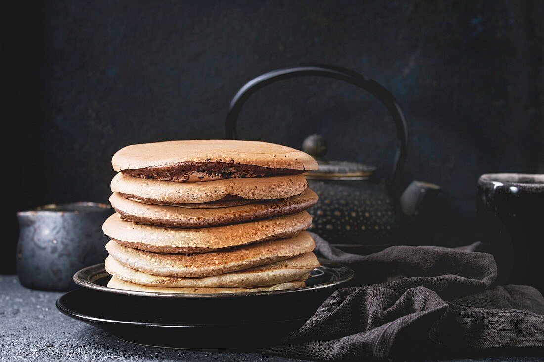 Ein Stapel Schokoladen-Pancakes auf Teller serviert mit Tee