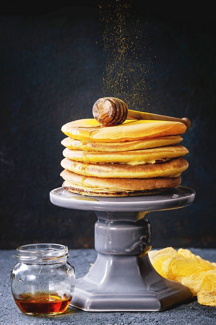 Stack of homemade american ombre yellow turmeric pancakes with honey sauce served on cake stand