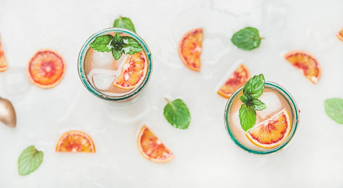 Blood orange fresh summer lemonade with ice and mint in glasses, light grey marble background