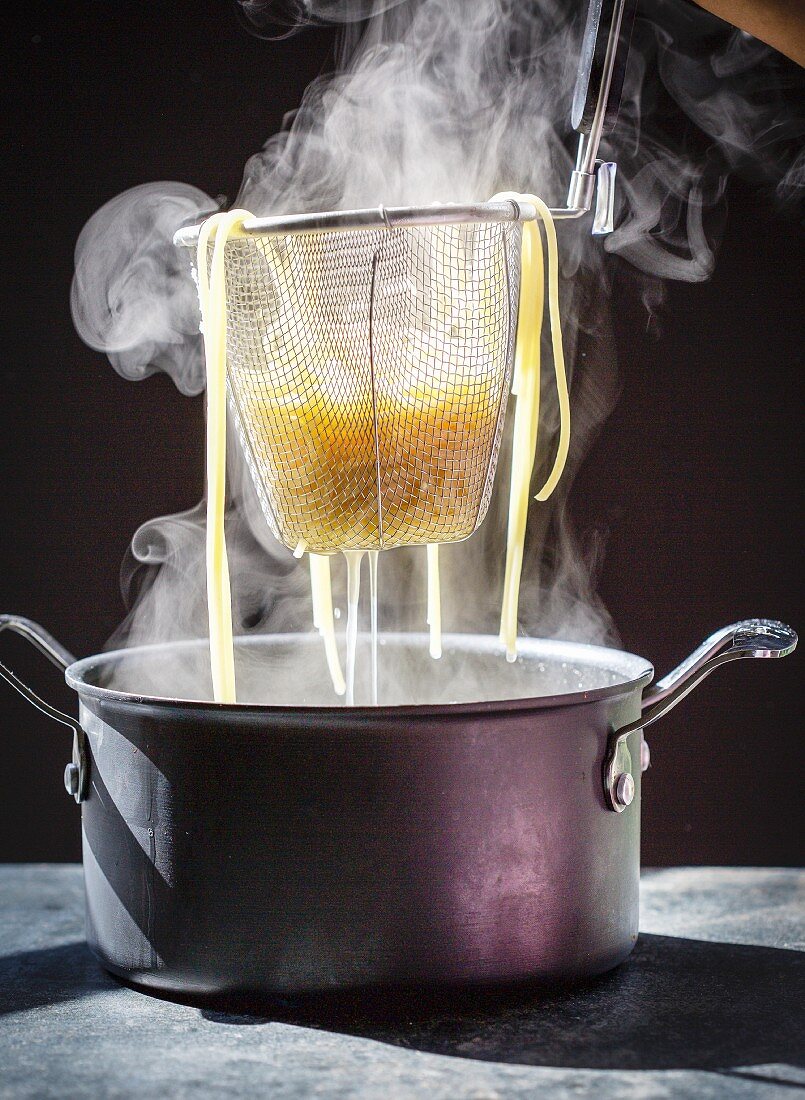Dampfende gekochte Pasta im Siebeinsatz über Topf abtropfen lassen