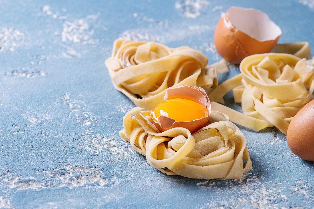 Selbstgemachte Pasta: Tagliatelle-Nester dazwischen Eierschalen und Eigelb
