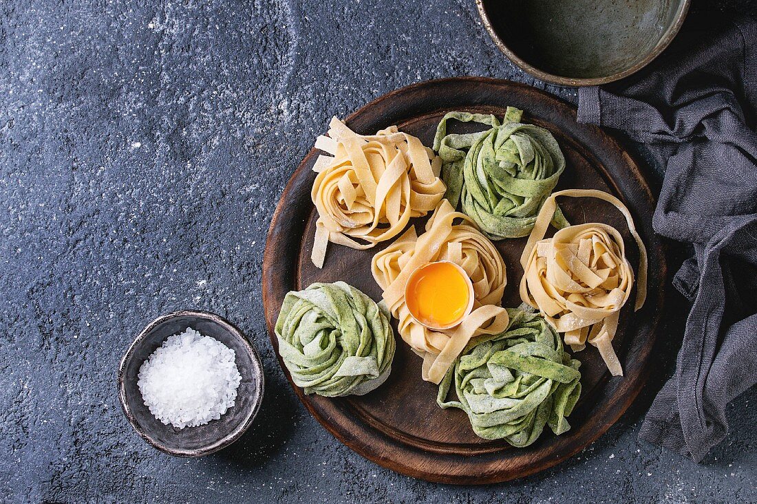 Variety of raw uncooked homemade pasta tagliatelle green spinach and traditional yellow with egg yolk