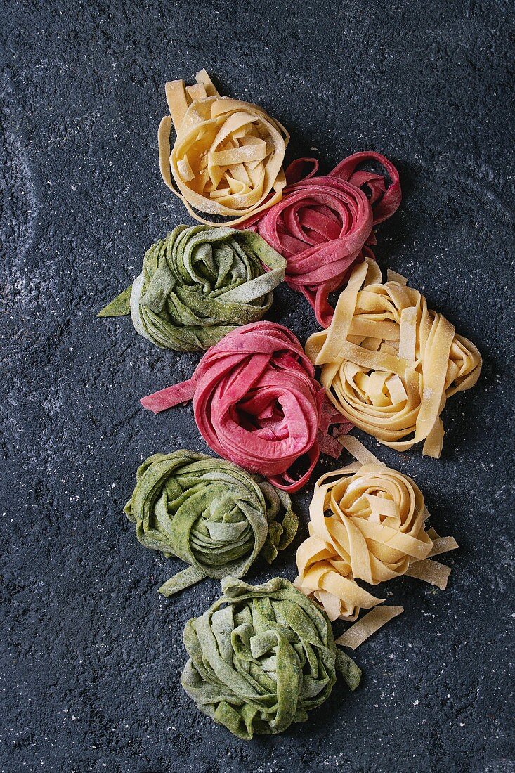 Variety of colored fresh raw uncooked homemade pasta tagliatelle green spinach, pink beetroot and traditional yellow