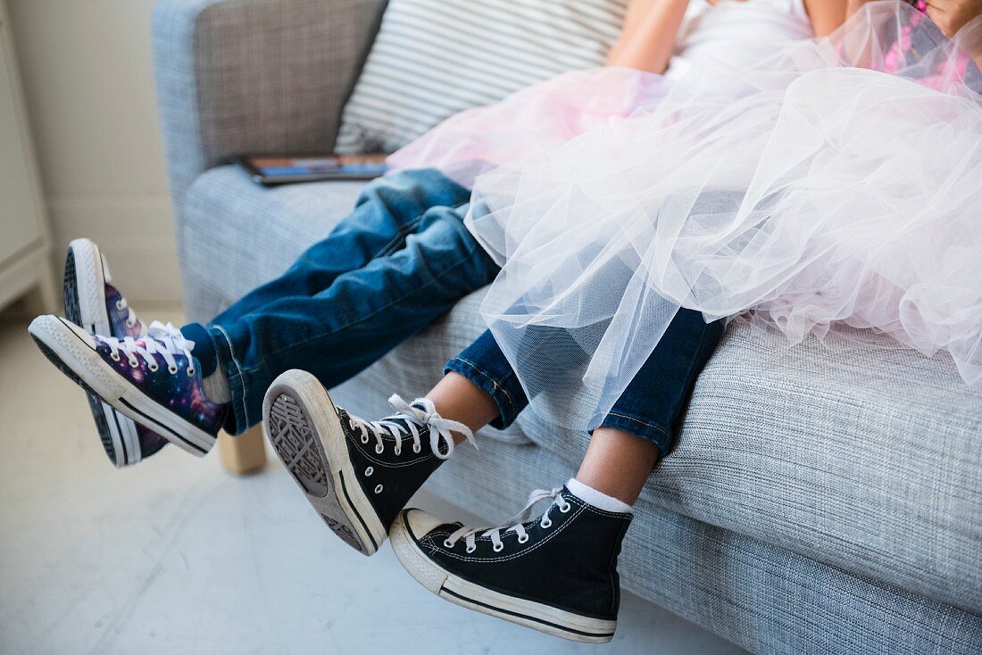 Legs of young girls wearing jeans, tutus and Chucks sitting on a sofa