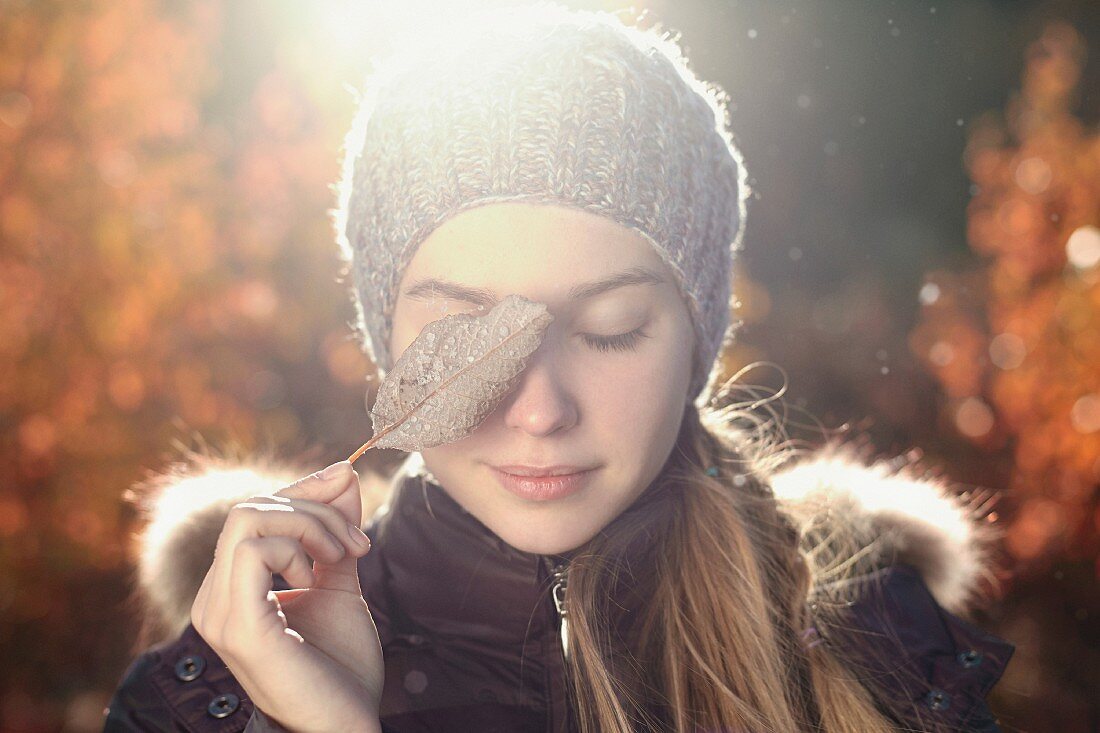 Junge Frau in Winterkleidung bedeckt ihr Auge mit einem Blatt