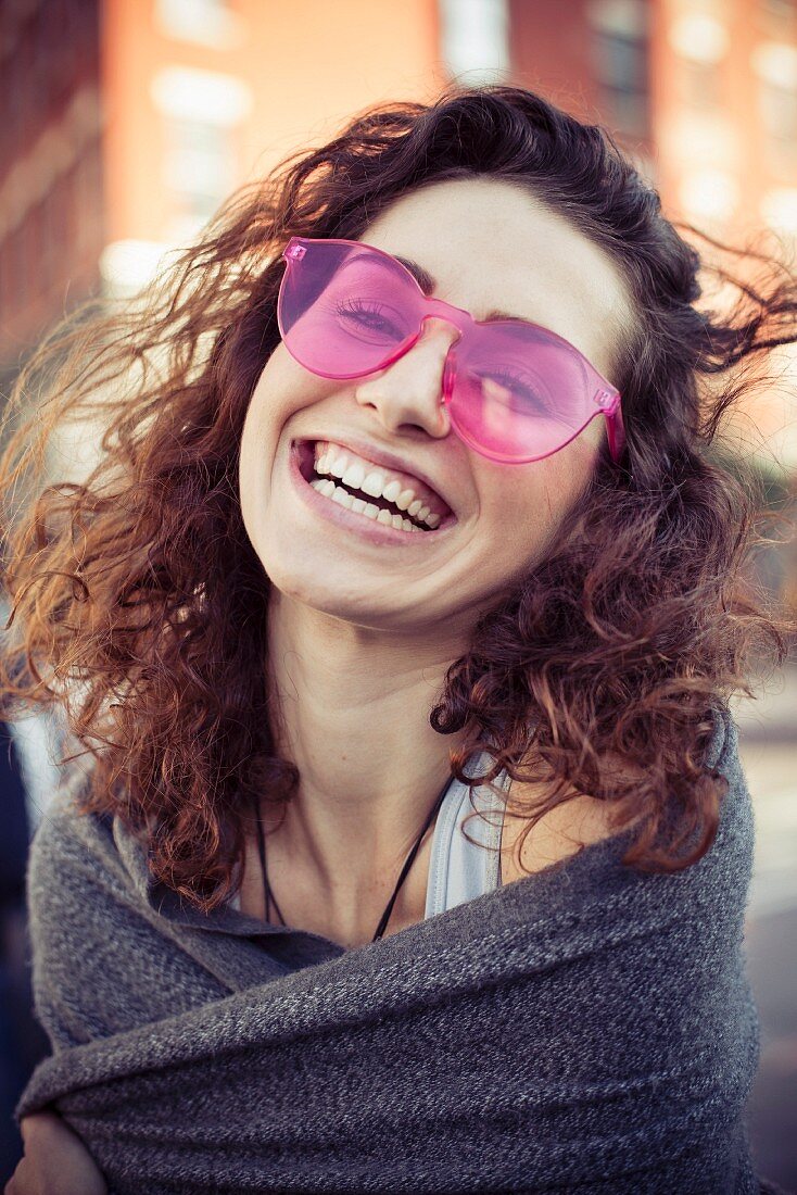 A brunette woman with curly hair wearing pink sunglasses