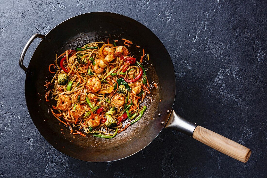 Udon stir-fry noodles with shrimp in wok pan on dark stone background