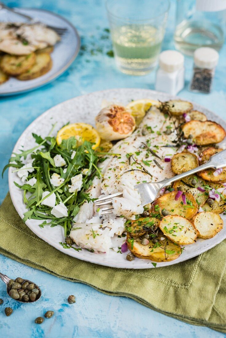 Oven-baked Barramundi fish fillet with crispy potatoes and rocket salad