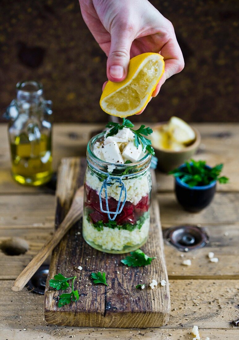 Lemon juice being squeezed on a millet and feta salad with beetroot and parsley in a glass jar