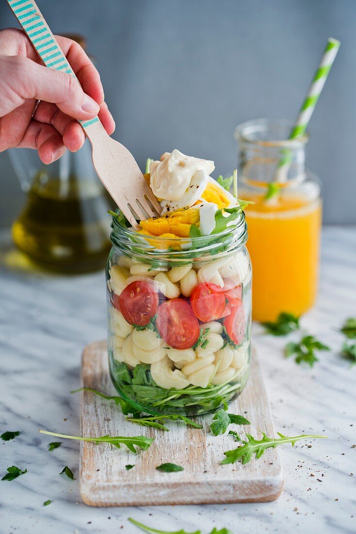 Pasta salad with tomatoes, egg and rocket in a glass jar