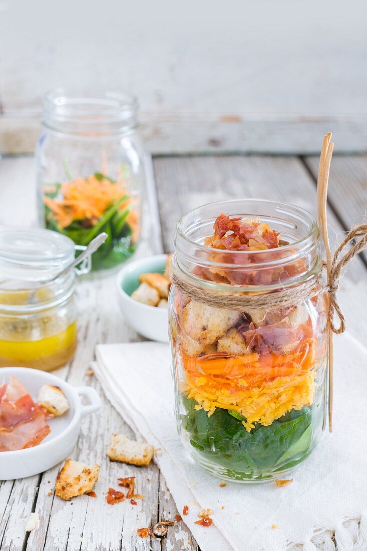 Bunter Salat mit Gemüse, Speck, Cheddar, Croûtons und Zitronen-Honig-Dressing im Glas