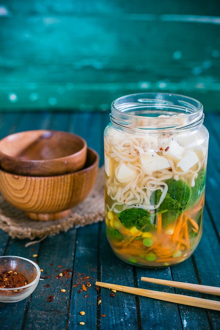Vegan noodle soup with vegetables and tofu in a glass jar
