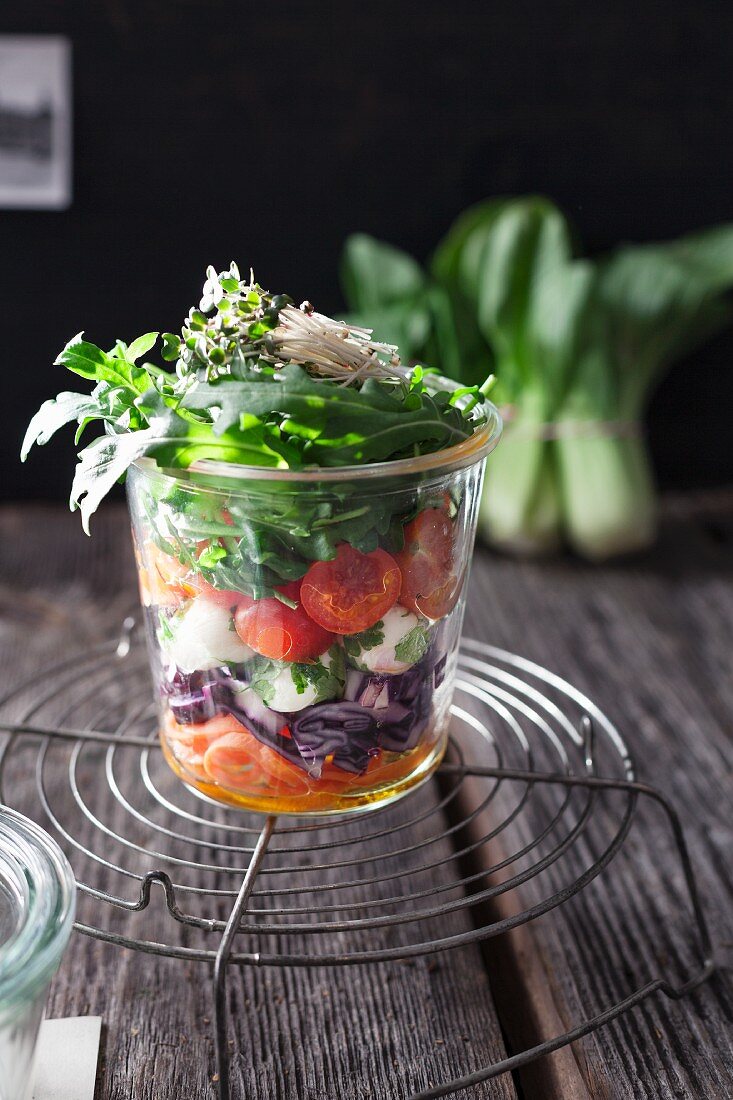 Layered salad with rocket, tomato, carrot, mustard cress, red cabbage, mozzarella, parsley and pak choi in a glass jar