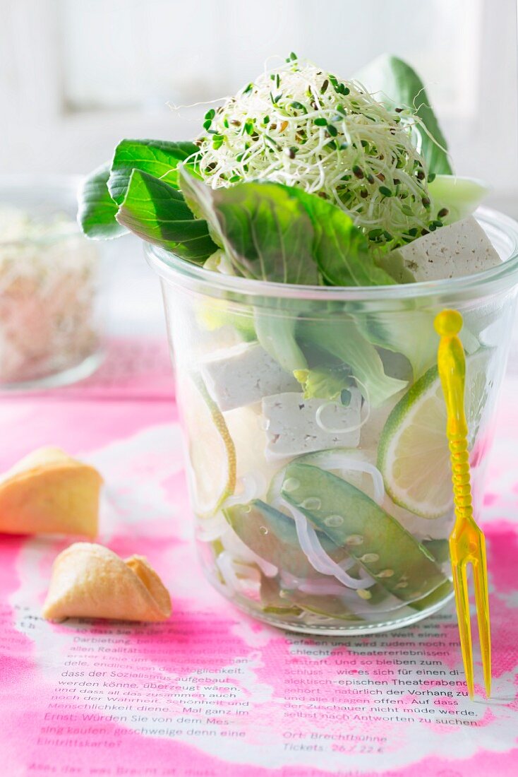 Salat mit Reisnudeln, Tofu, Erbsenschoten, Pak Choi und Sprossen im Glas, daneben Glückskeks (Asien)