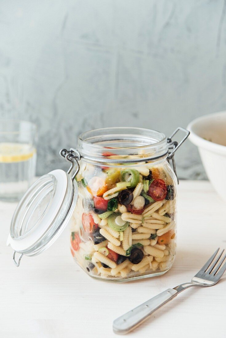 Mediterraner veganer Nudelsalat im Glas mit Kirschtomaten, Frühlingszwiebeln, Basilikum und Oliven