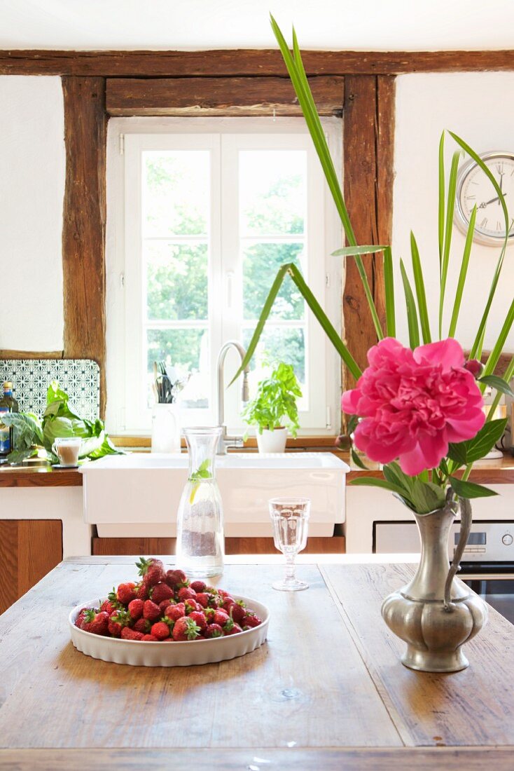 Strawberries, carafe of water and pewter vase of peonies on kitchen table