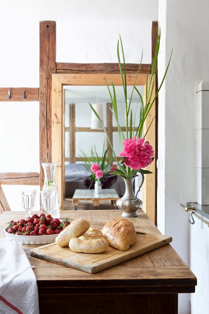 Brötchen auf Schneidebrett, Erdbeeren und Pfingstrose auf Holztisch