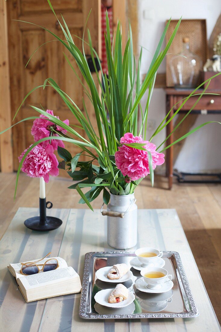 Pastries and tea on tray next to book and pink peonies on table