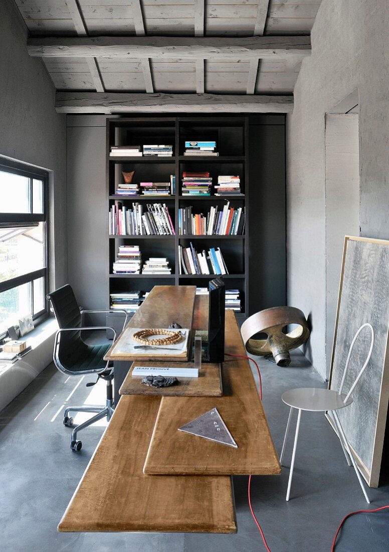 Schreibtisch mit verschiedenen Upcycling-Tischplatten vor schwarzem Bücherregal in Büro