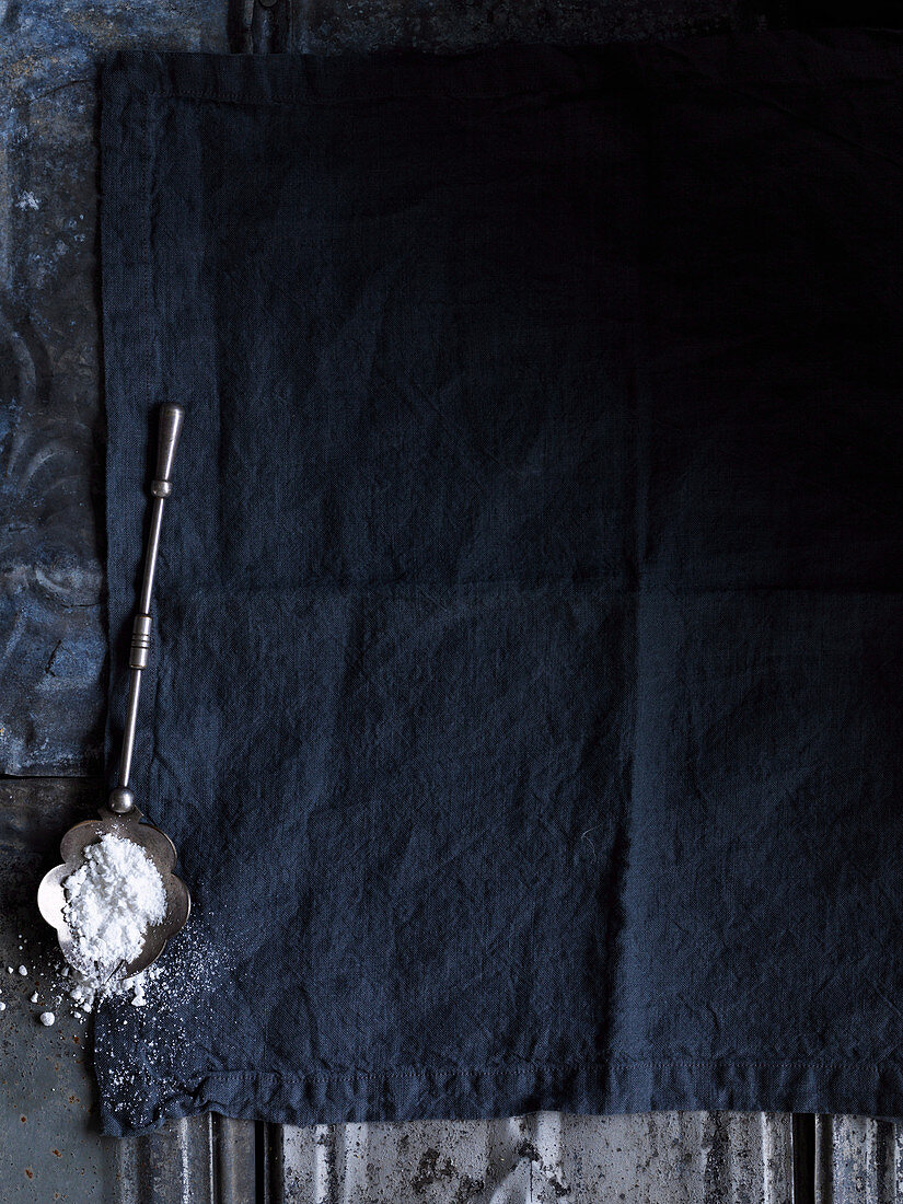 Antiker Löffel mit Puderzucker auf dunkelblauem Stoffgrund