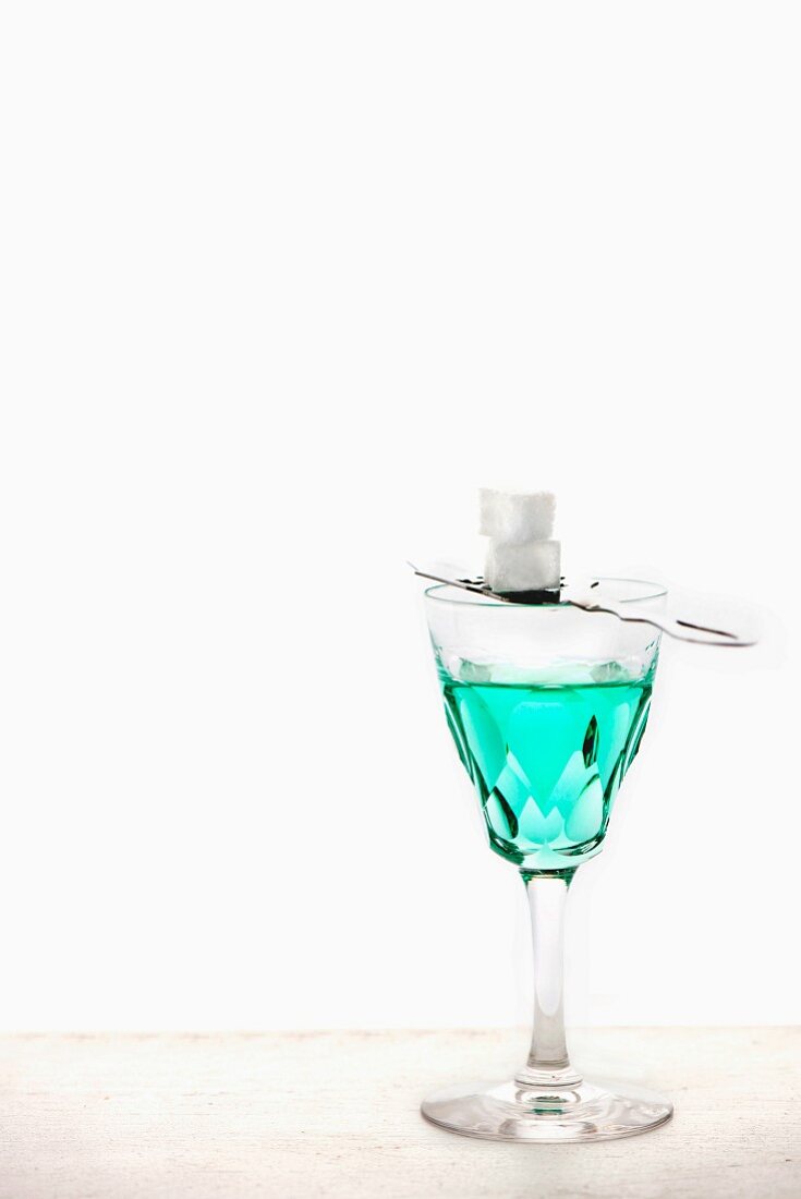 Absinth mit Absinthlöffel und Zuckerwürfel im Kristallglas