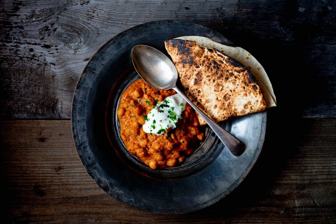 Chana Masala (Indian chickpea curry) on a tin plate with chapati and yoghurt dip