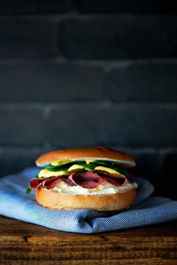 A bagel with cream cheese, pastrami, lettuce and mustard mayonnaise