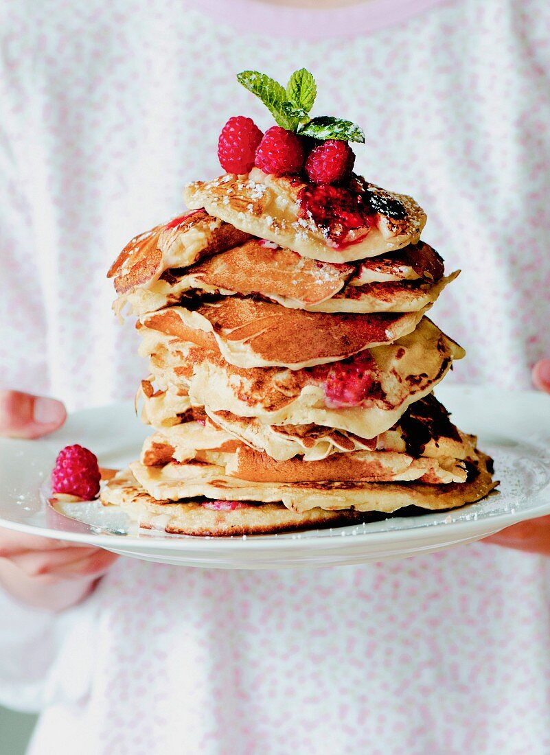 A stack of homemade vanilla and raspberry pancakes on a white plate