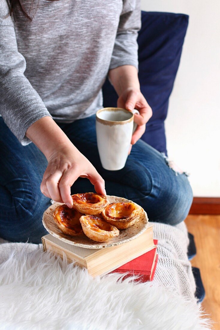 Frau mit Tasse Kaffee und Pastel de Nata (Eiertörtchen, Portugal)