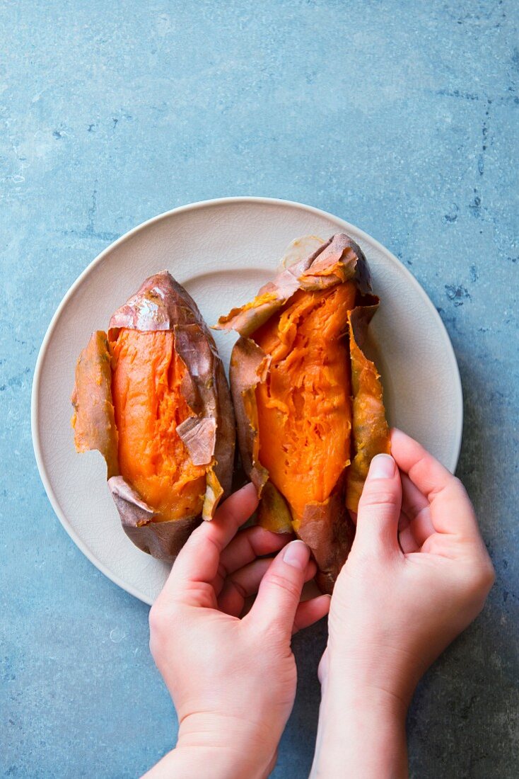 Female hands peeling freshly baked sweet poatoes