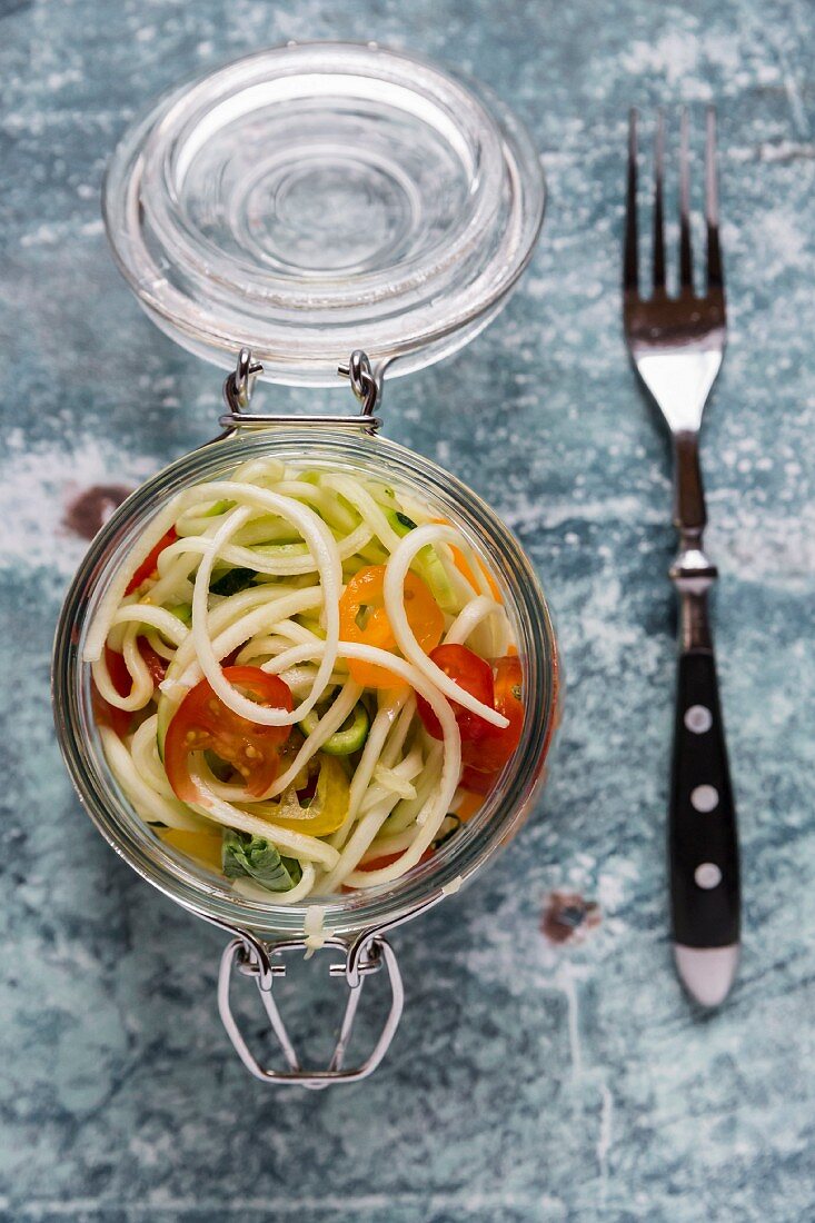 Zoodles (zucchini noodles) in a glass jar with tomatoes and basil