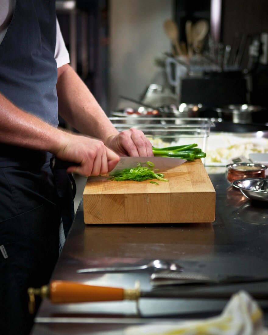 A chef chopping spring onions in a restaurant kitchen