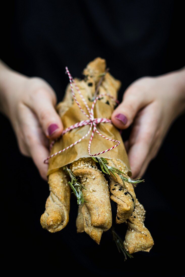 A woman's hands holding homemade bread sticks with rosemary and sesame seeds