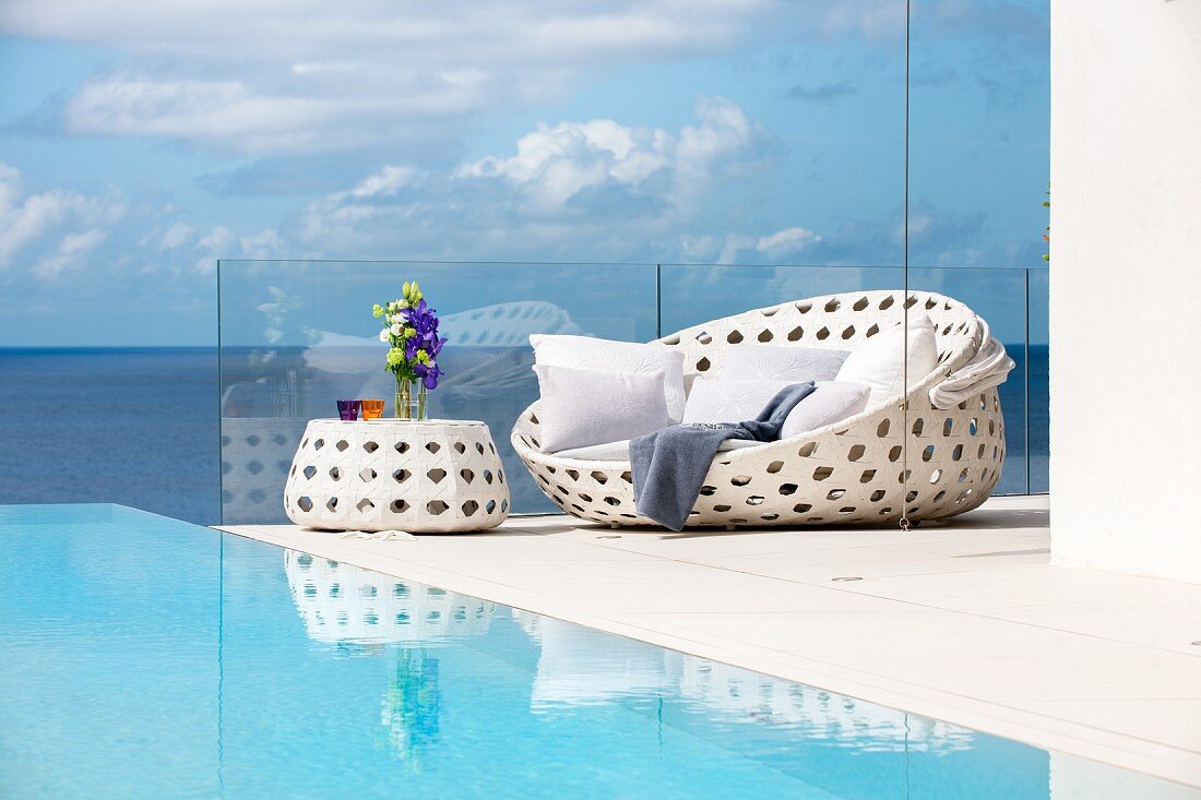 weiße Outdoormöbel am Pool mit Blick aufs Meer und Wolkenhimmel