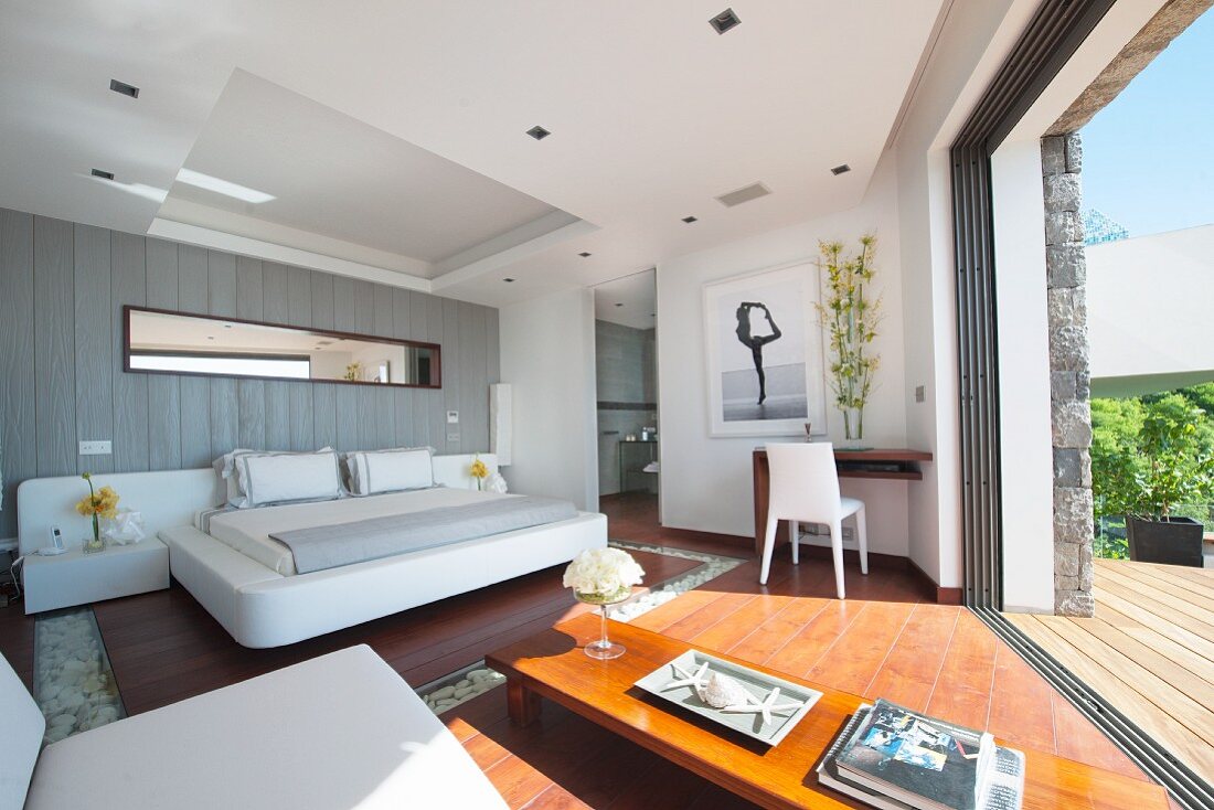 Luxurious bedroom with open glass wall leading to terrace